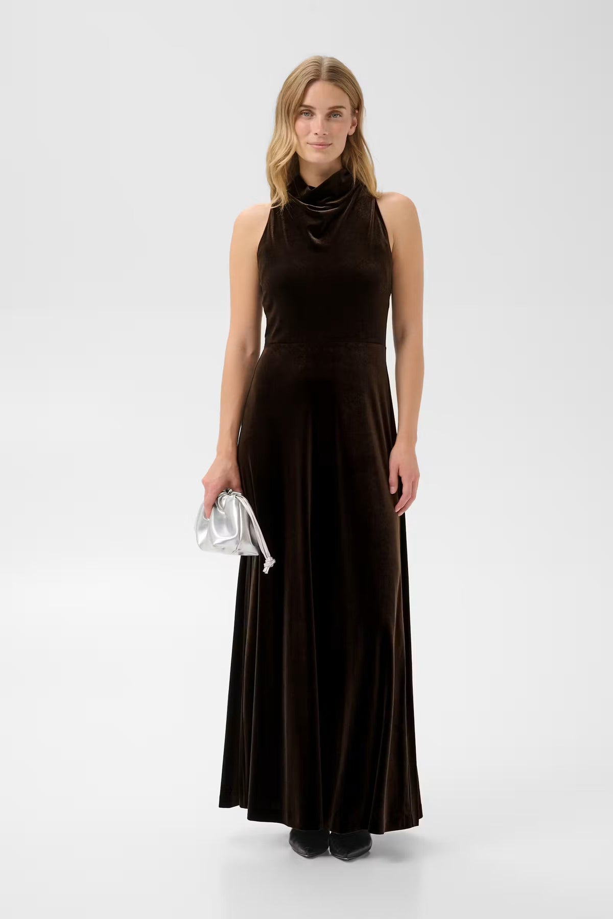 Model wearing Part Two Dicle velvet maxi dress in mole brown with cowl neck and silver clutch