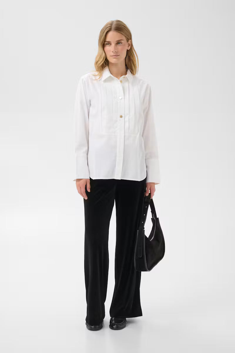 Black wide-leg velvet pants styled with a white button-up shirt and black bag.