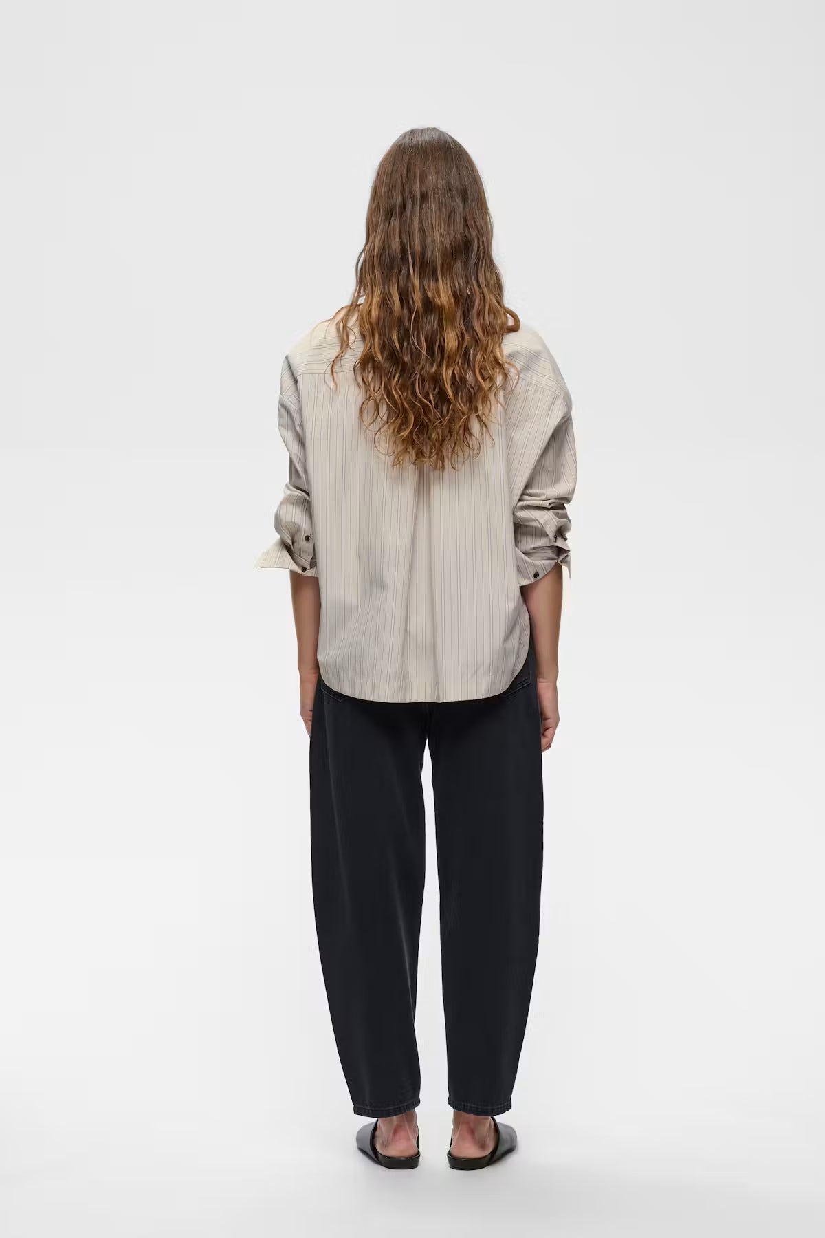 Beige pinstripe button-up shirt with rolled sleeves, worn with black wide-leg jeans, back view.