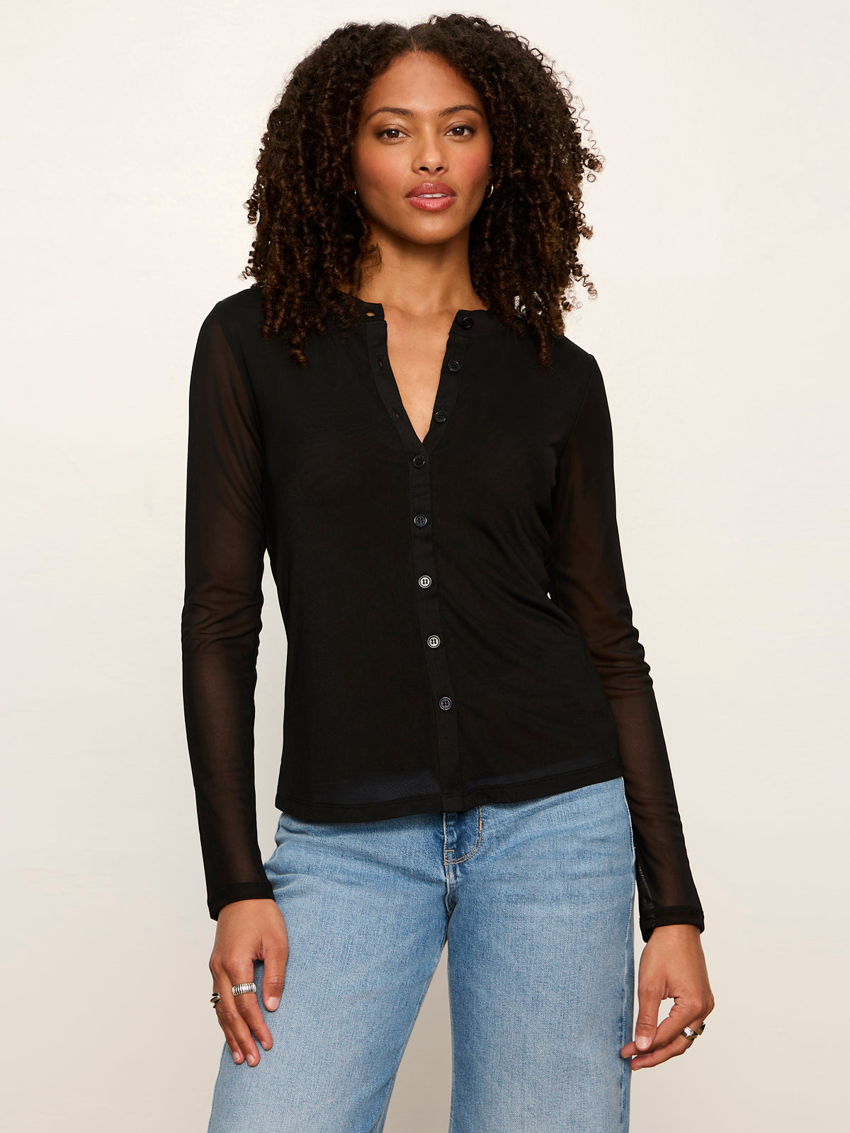 Woman wearing black mesh long sleeve button-front cardigan with sheer sleeves paired with blue jeans