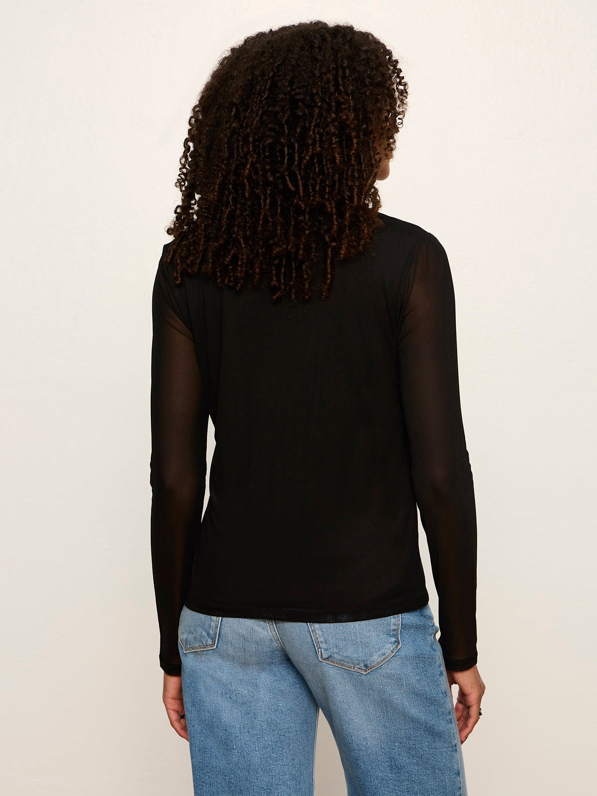 Back view of model wearing black mesh long sleeve cardi with sheer sleeves and blue jeans