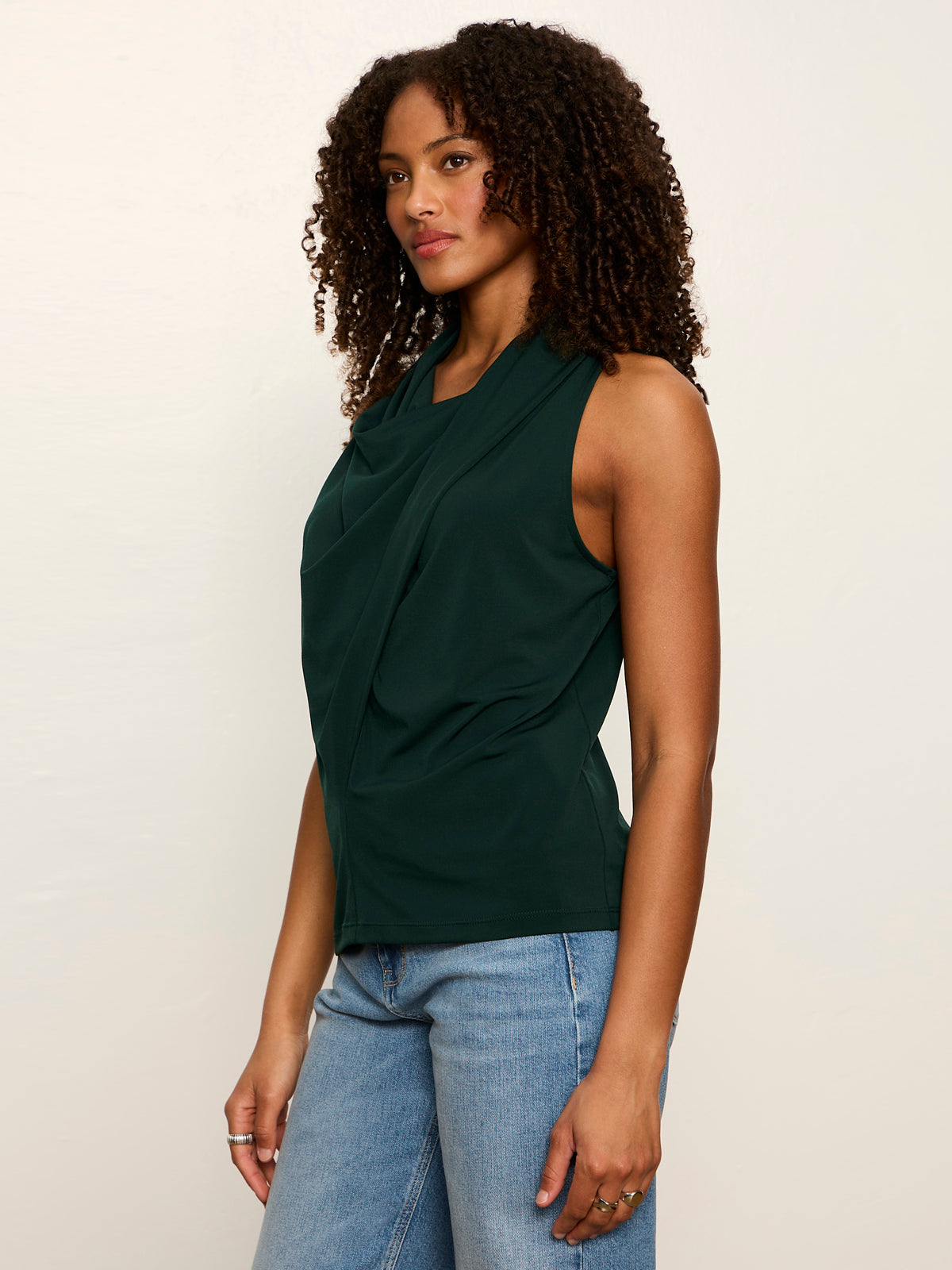 Woman wearing Sanctuary Nora Draped Tank in forest green with blue jeans, side view