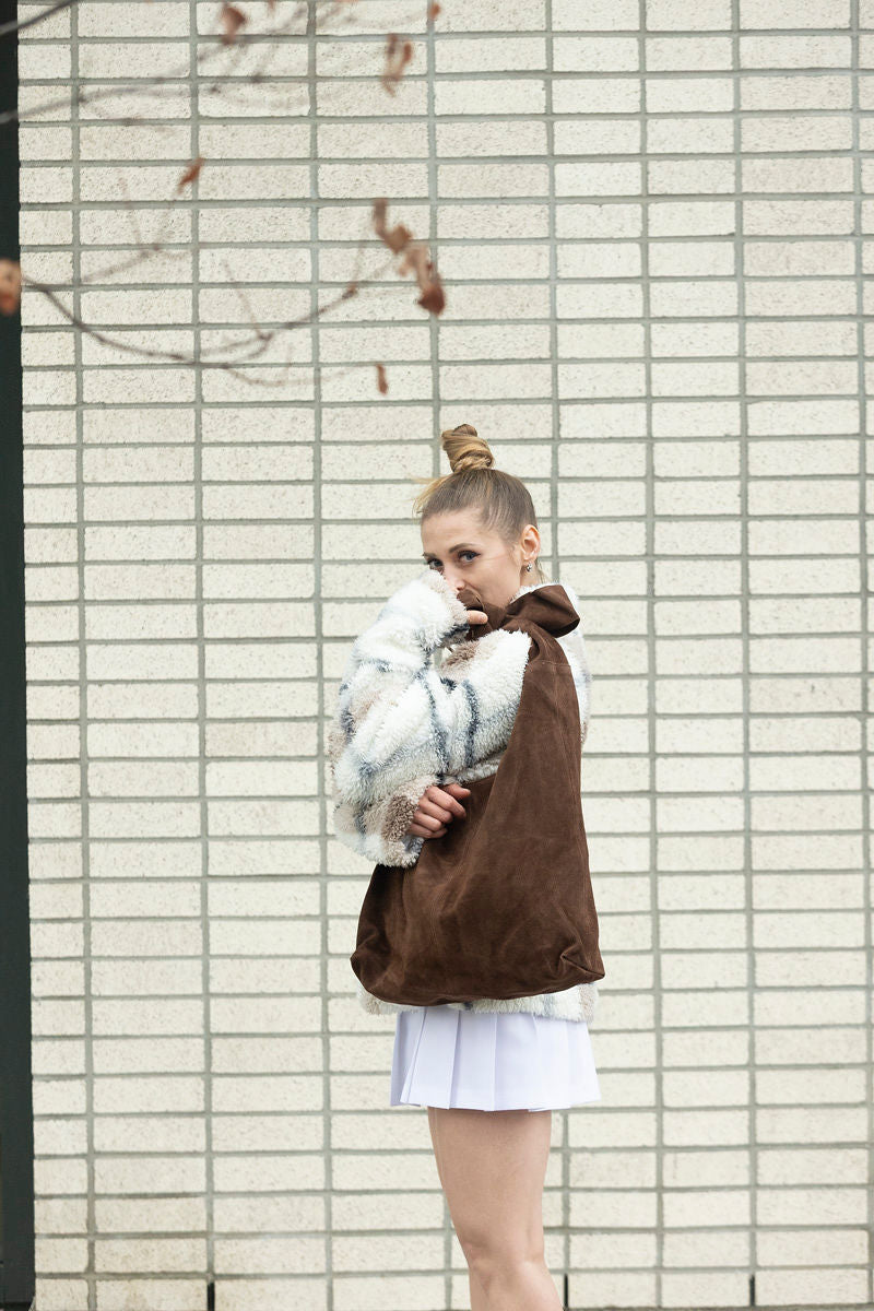 Brown suede knot tote bag held by model wearing fur jacket and white skirt