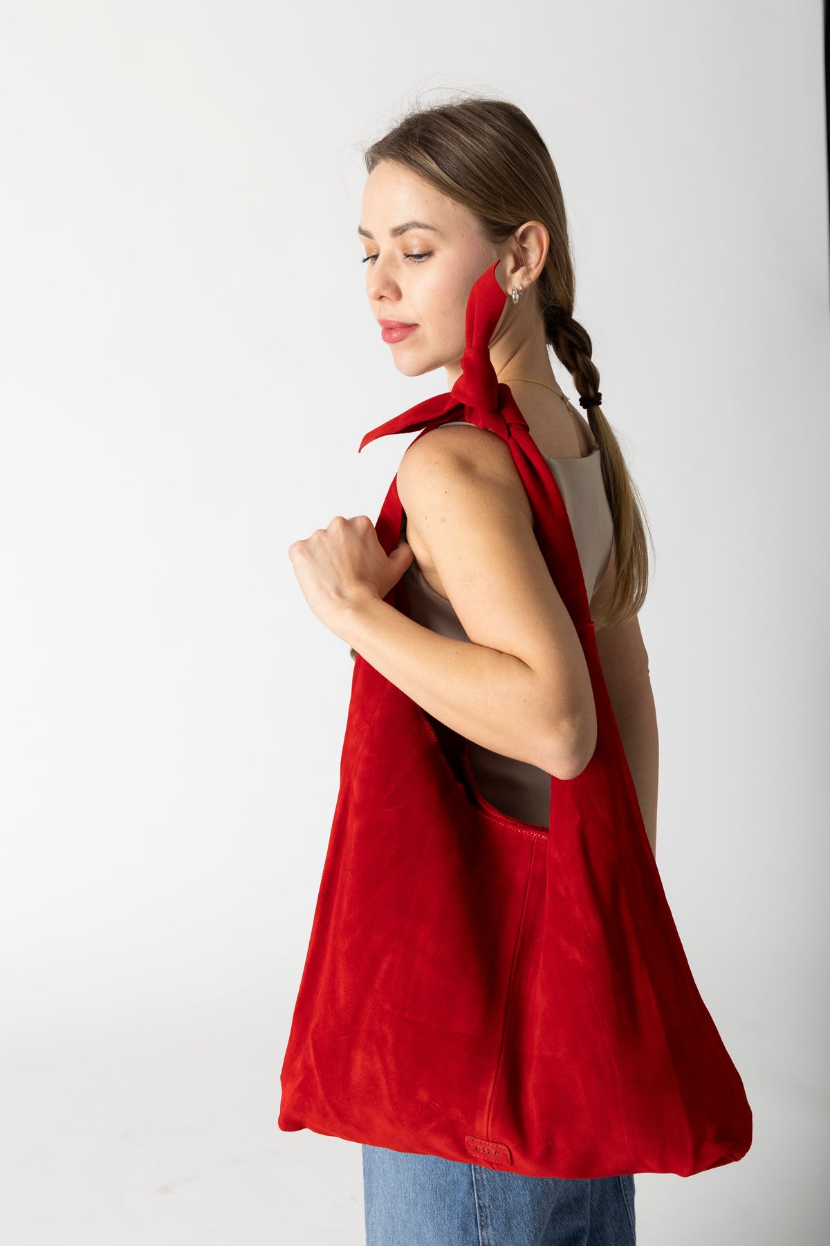Model carrying RISA Knot Tote Suede bag in red over her shoulder, side view