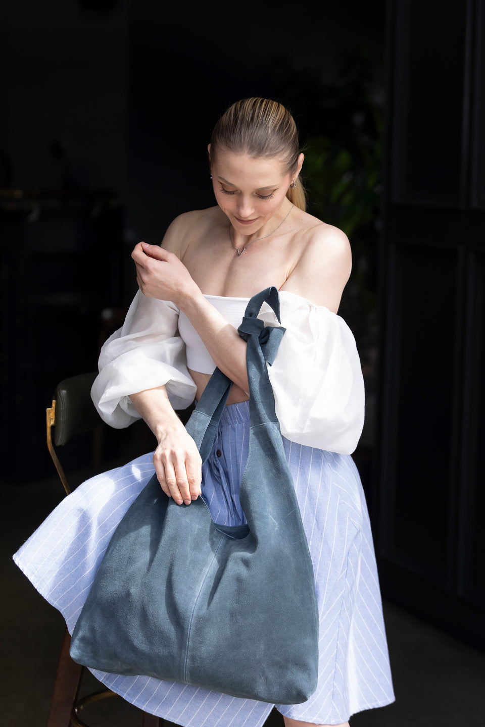 Blue suede hobo tote bag with knotted strap held by woman in white top