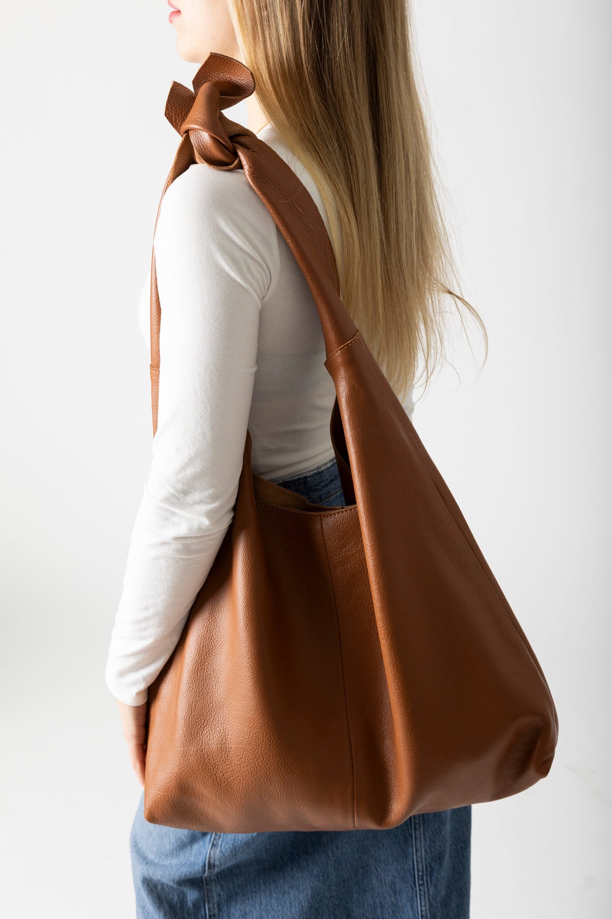 Model carrying RISA Knot Tote Leather bag in tan over shoulder, side view