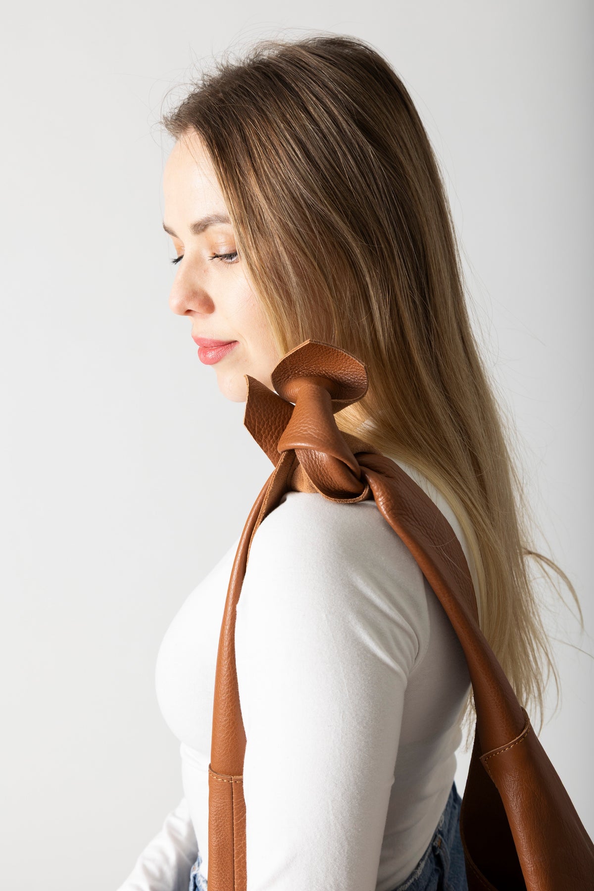 Woman wearing RISA Knot Tote leather bag in tan over her shoulder, side profile view