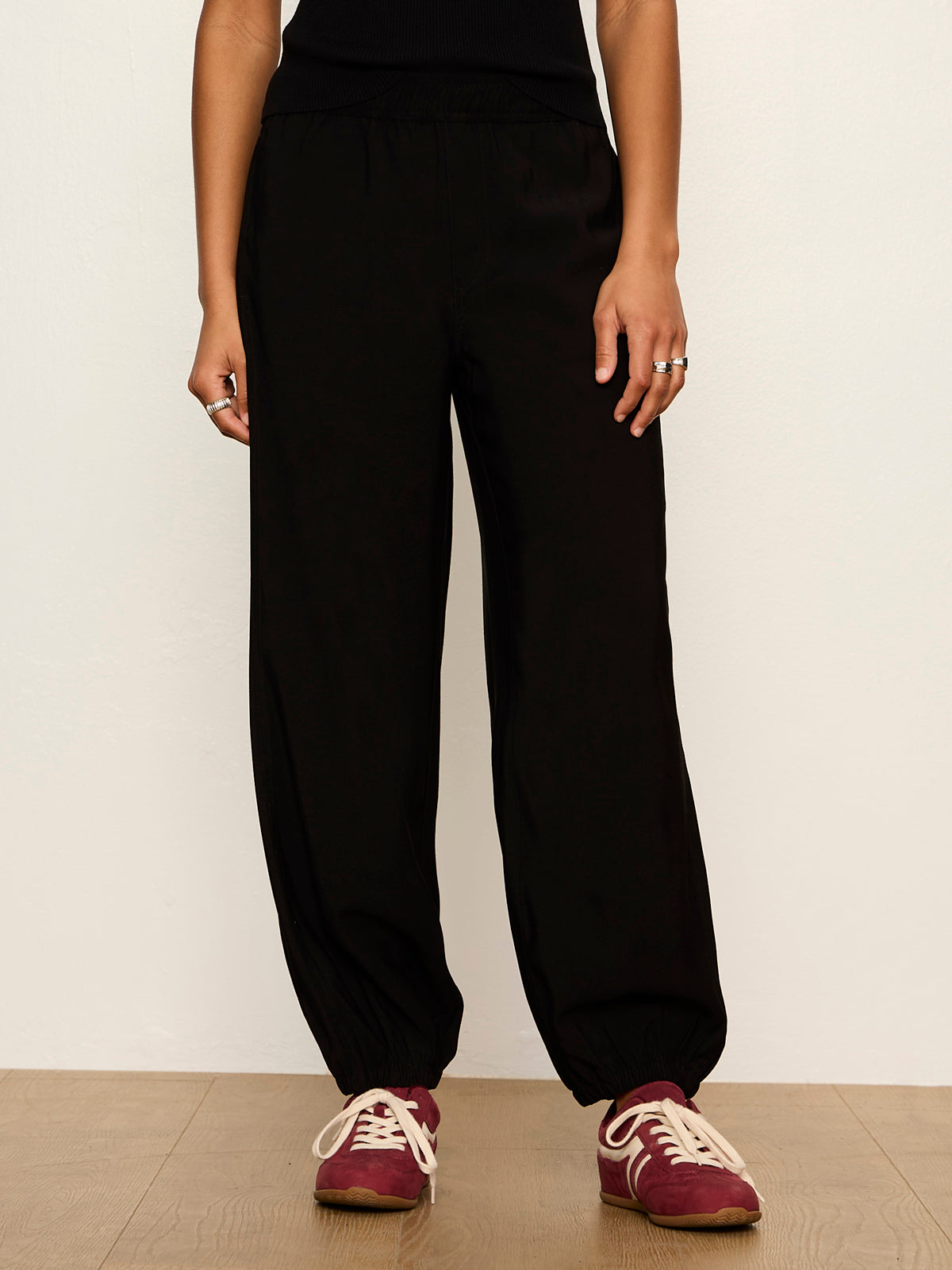 Model wearing black Sanctuary Micro Balloon Pants with elasticated cuffs and burgundy sneakers