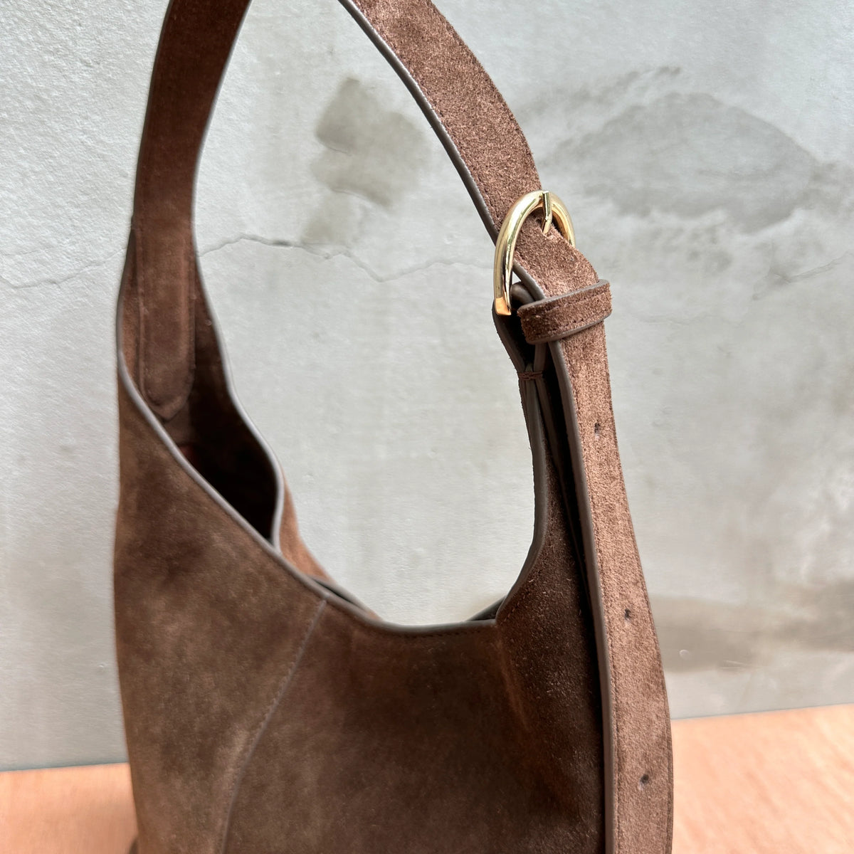 Chocolate brown suede shoulder bag with gold buckle detail and crescent silhouette