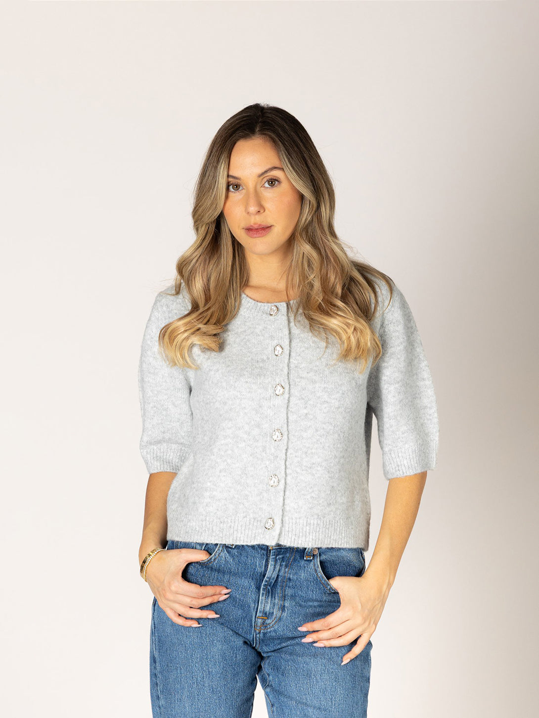 Woman wearing light grey short-sleeve knit cardigan with jewel buttons and blue jeans