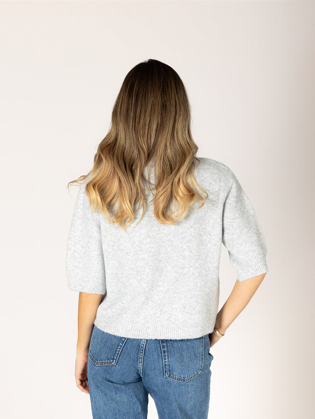 Back view of model wearing light grey short-sleeve knit cardigan with blue jeans