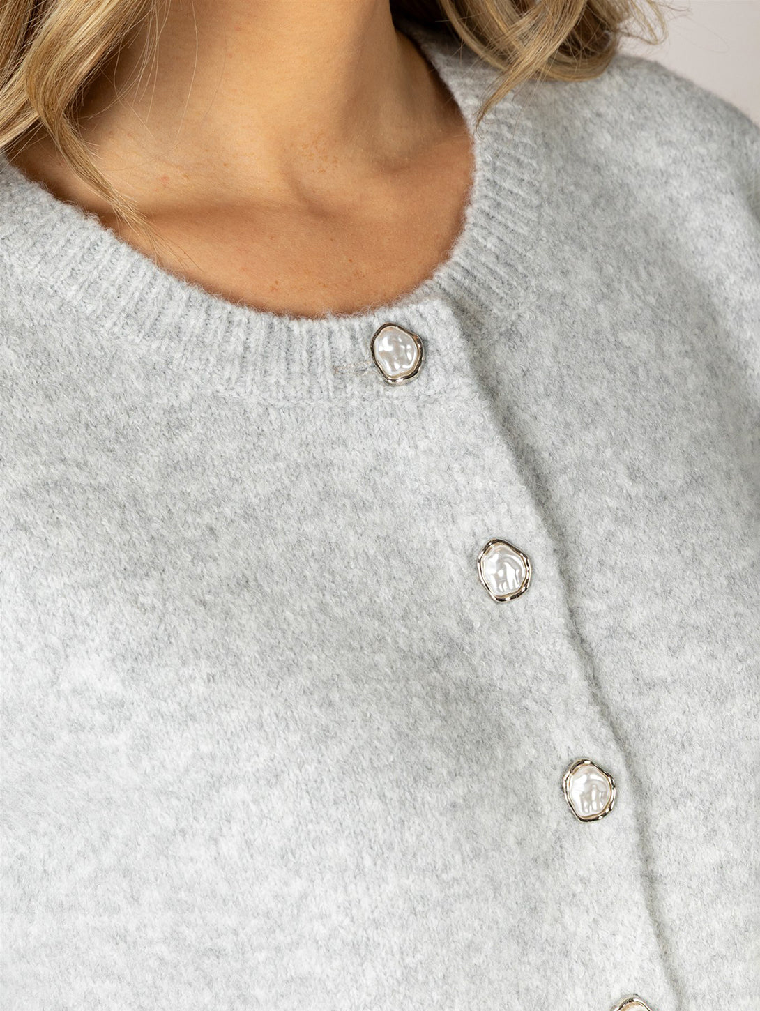 Close-up detail of light grey knit cardigan with decorative pearl and silver buttons