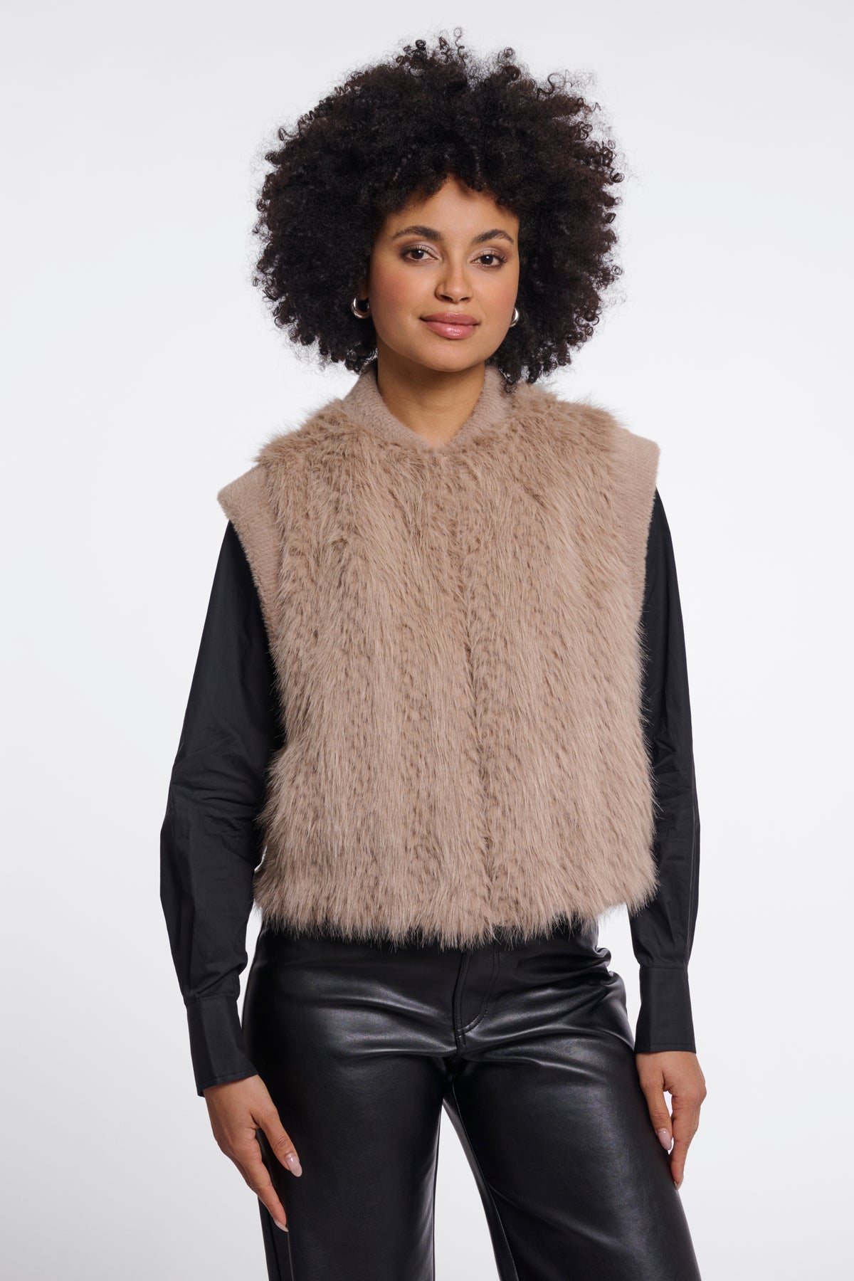 Beige faux fur sleeveless vest with crew neck worn over black leather shirt and trousers