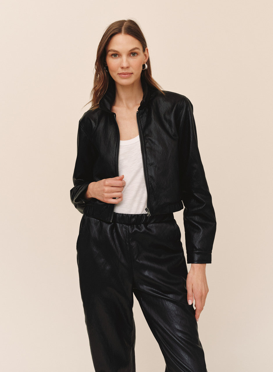Woman wearing black faux leather crop bomber jacket with white tank top and matching pants
