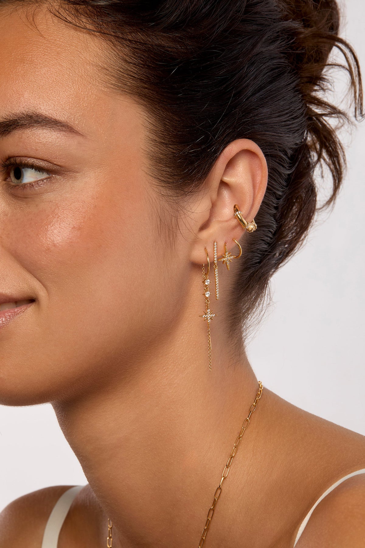 Model wearing gold star charm drop earrings with crystal accents and ear cuff set