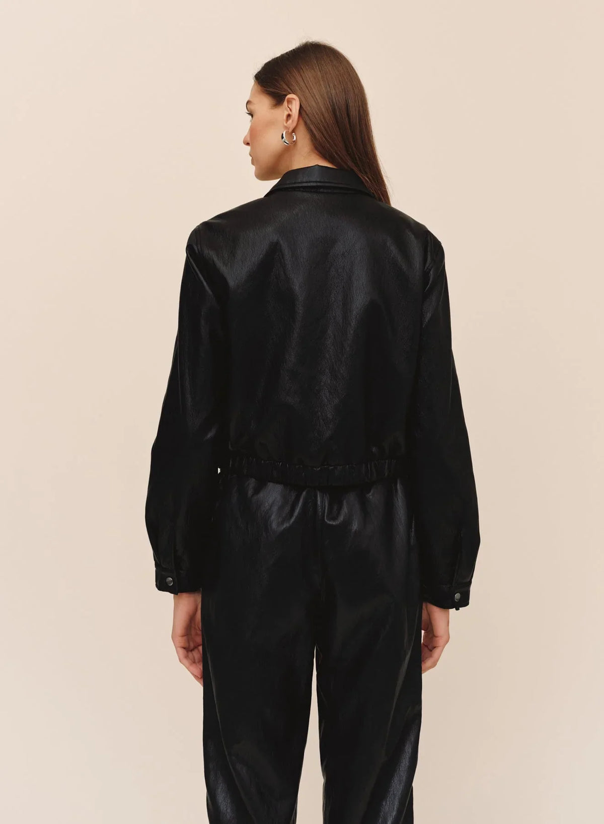 Back view of black faux leather crop bomber jacket with elastic hem on female model