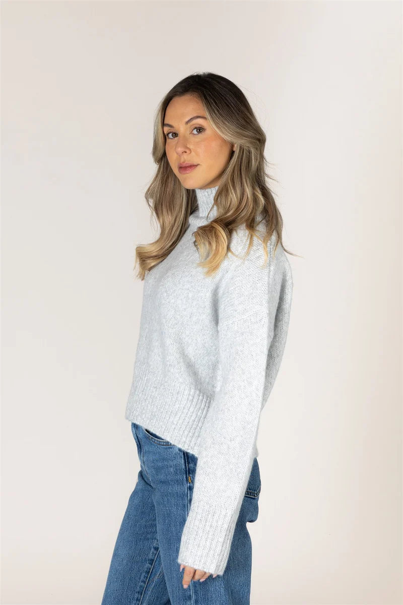 Light grey turtleneck knit sweater with ribbed cuffs and hem, paired with blue jeans