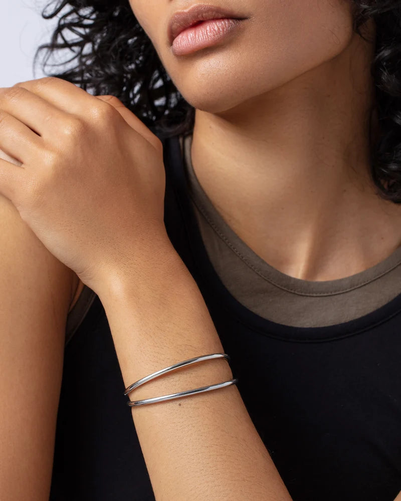 Two slim silver bangle bracelets stacked on a model's wrist