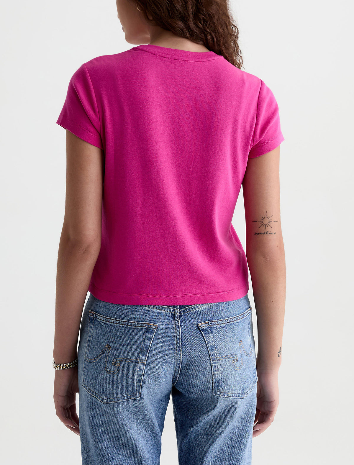 Back view of model wearing AG Sadie Crew short-sleeve tee in bright pink with blue jeans