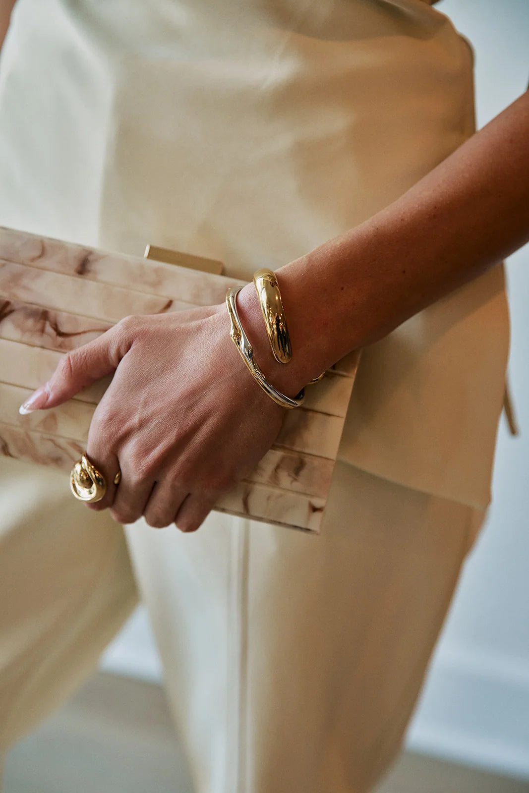 Gold sculptural cuff bangle worn on wrist, paired with gold ring and clutch