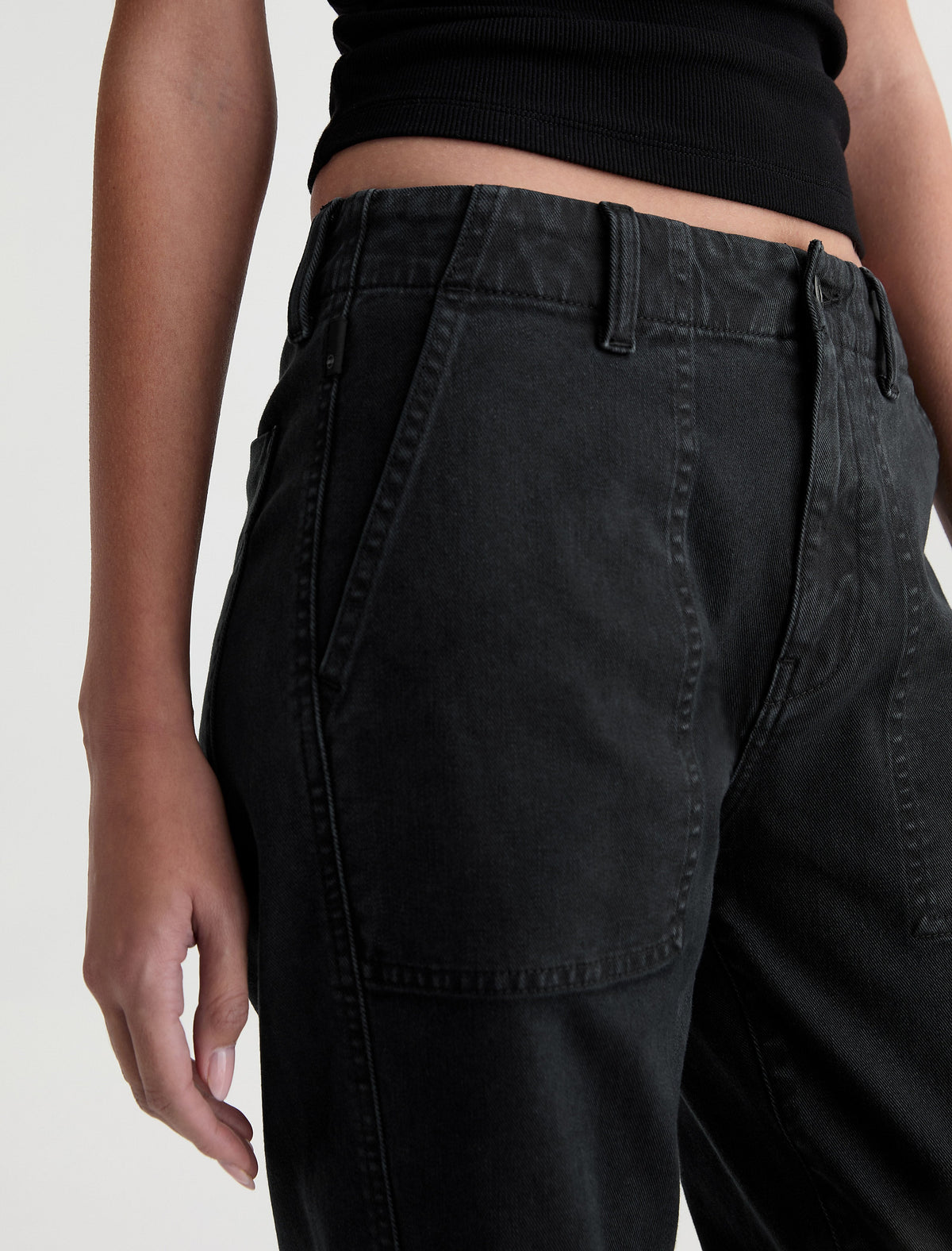 Close-up detail of AG Analeigh Sulfur Super Black pants showing front patch pocket and waistband