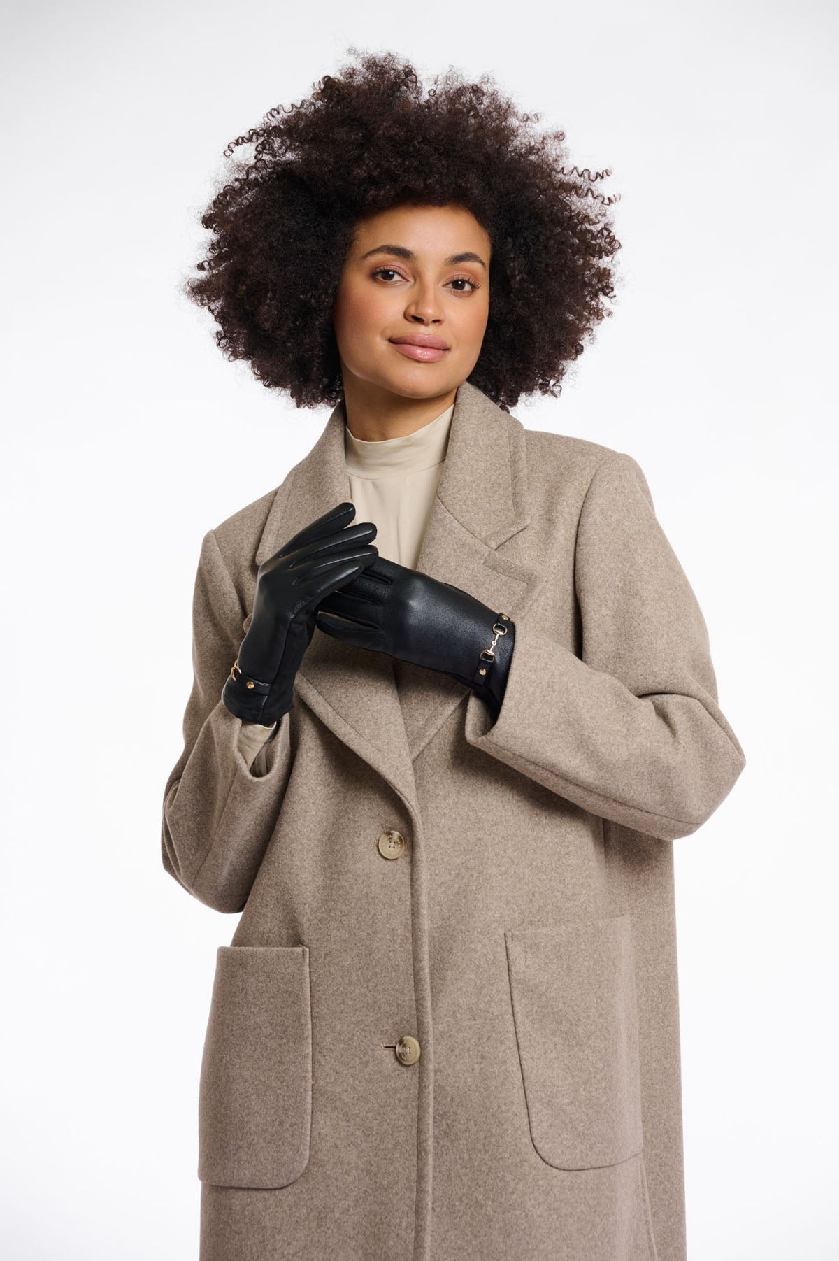 Model wearing black leather gloves with gold hardware detail paired with beige wool coat