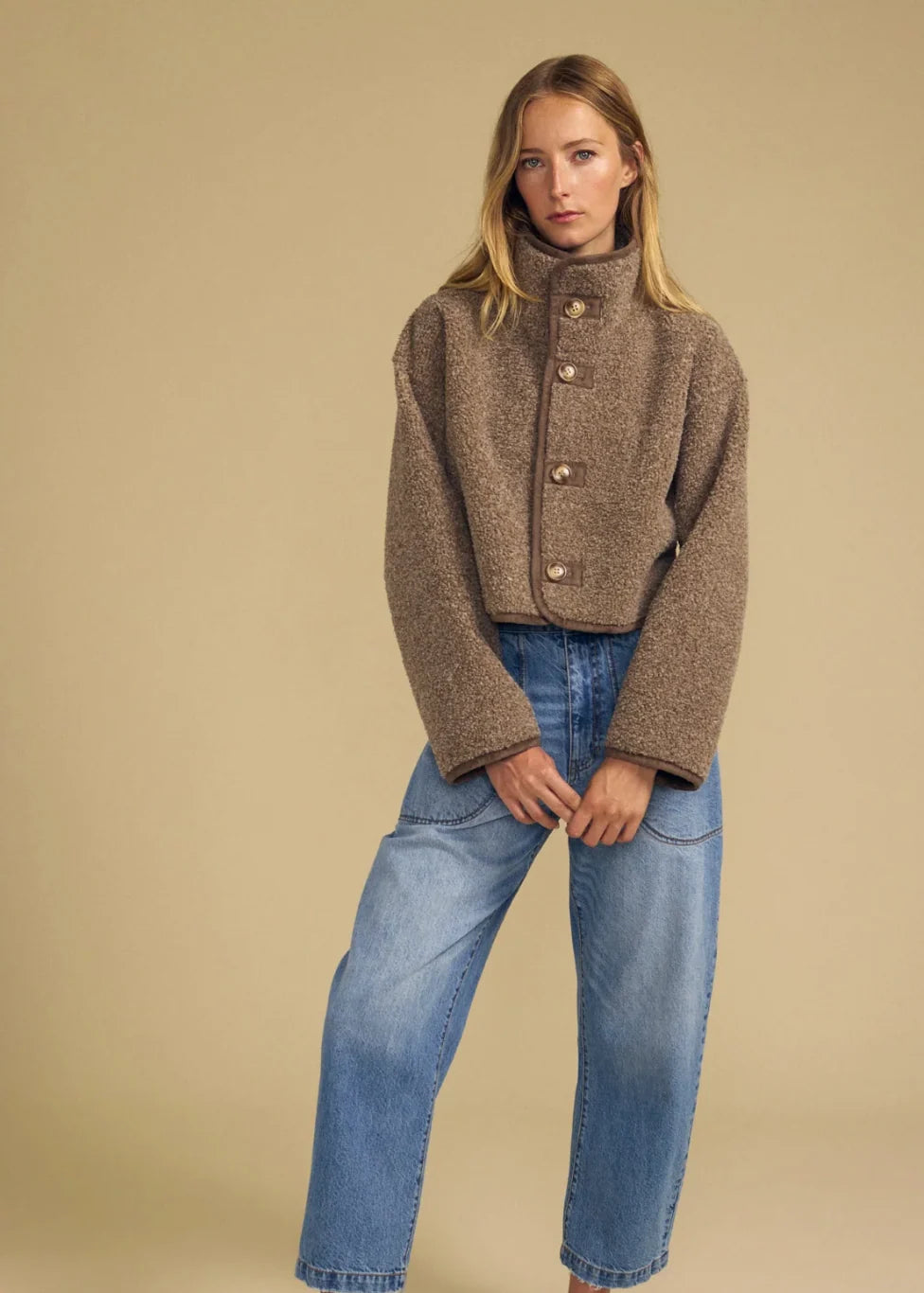 Cropped brown bouclé jacket with gold buttons and high neck, styled with wide-leg jeans.