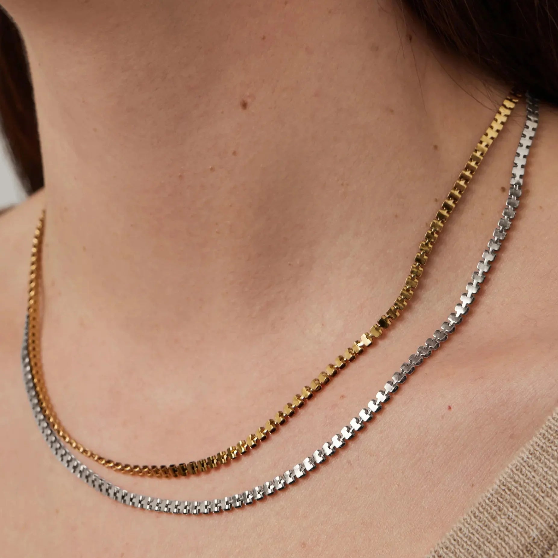 Two-tone box chain necklace layered in gold and silver on a woman's neck