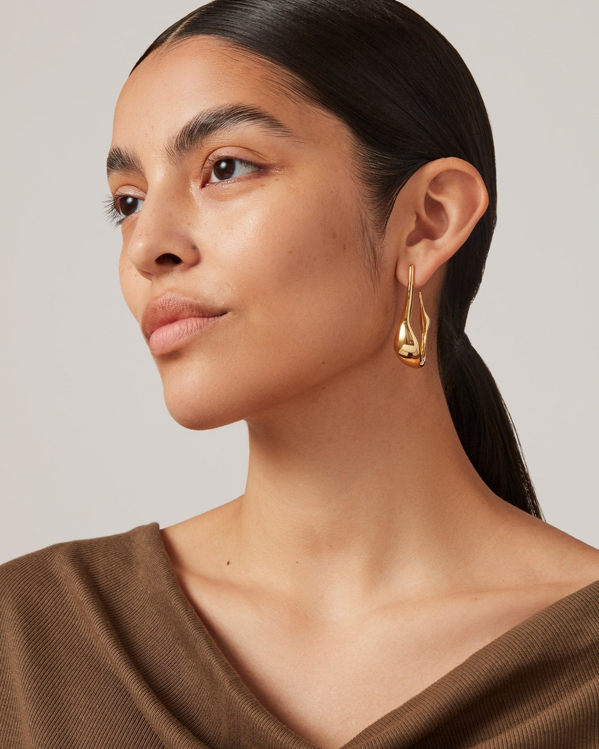 Model wearing Jenny Bird Egret Hoops gold sculptural drop earrings, three-quarter view