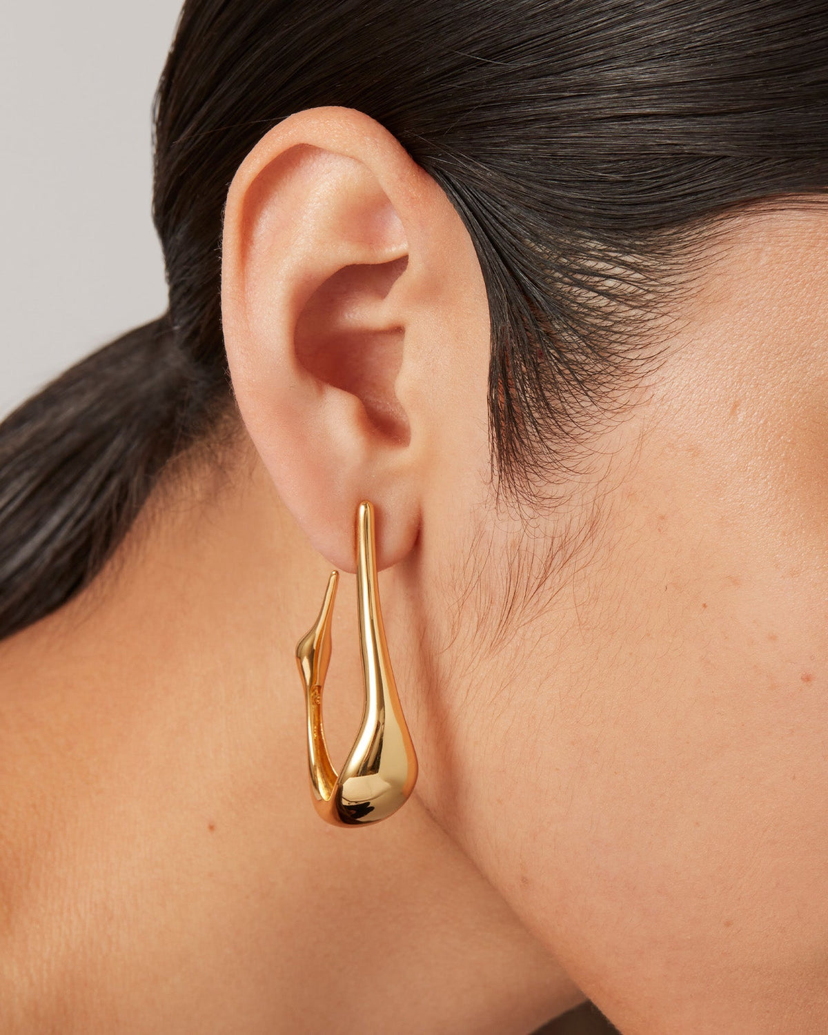 Model wearing Jenny Bird Egret Hoops gold open-loop earring shown in close-up side profile