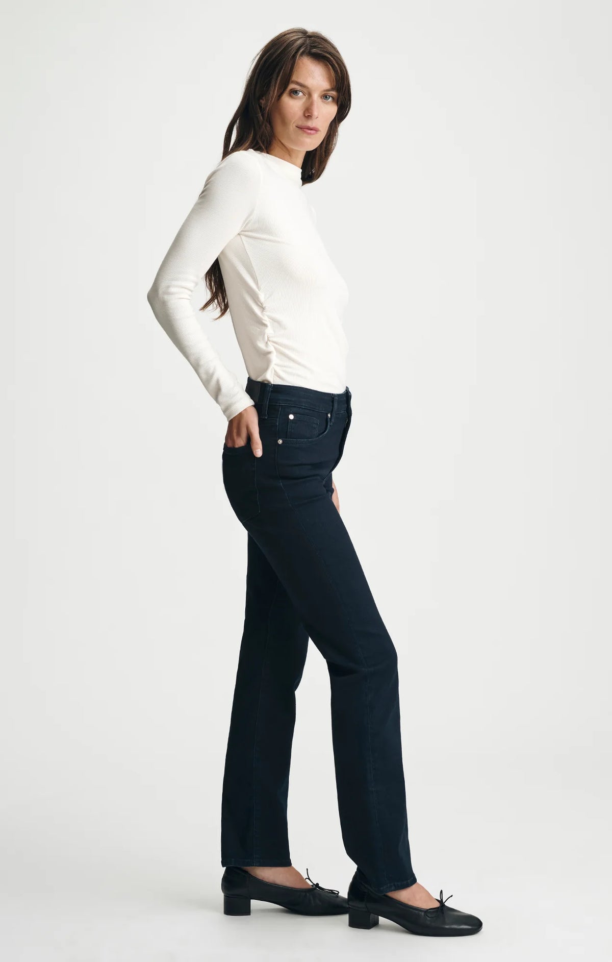 Woman wearing dark navy straight-leg jeans with white long-sleeve top and black flats