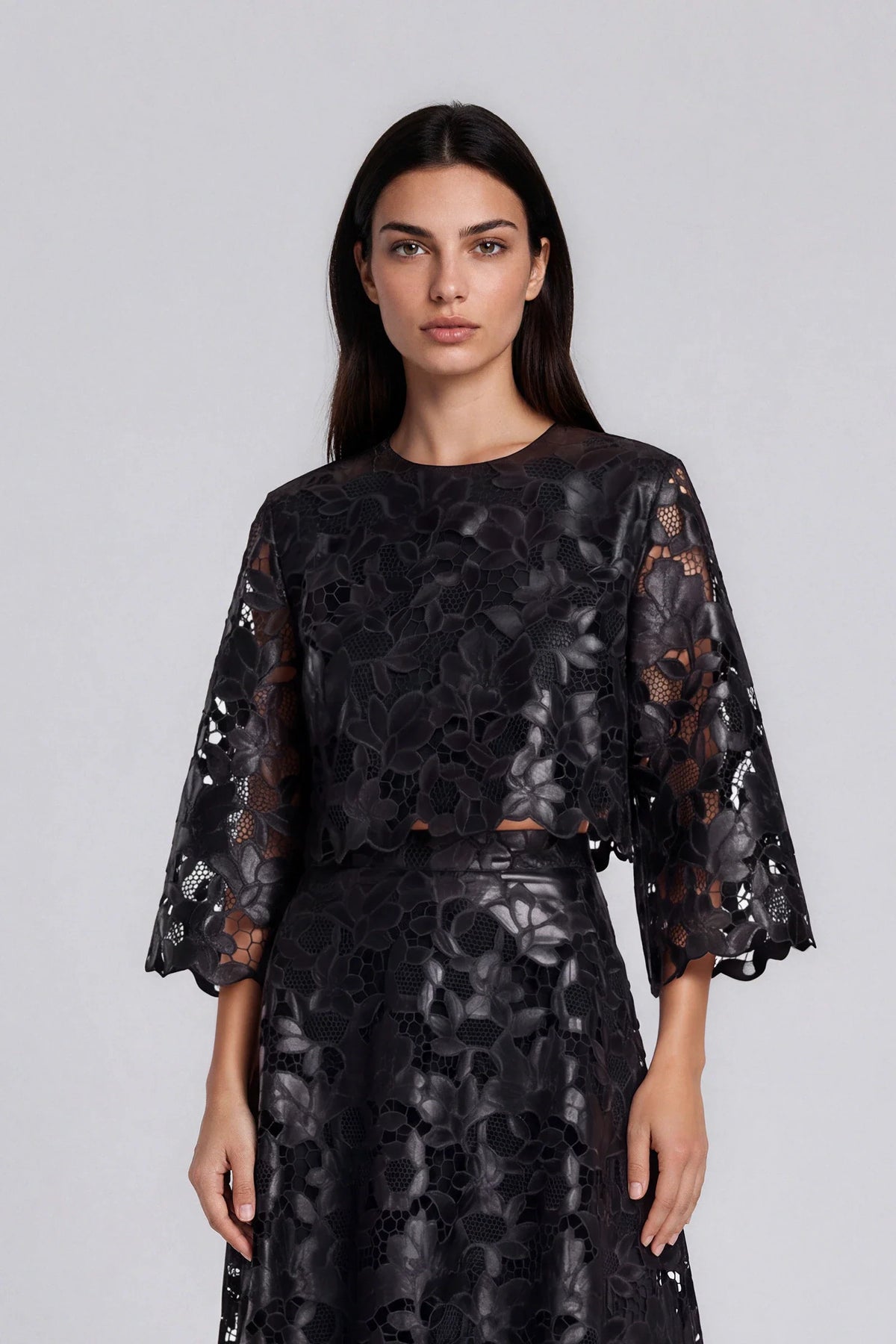 Model wearing black floral lace bell sleeve cropped top with scalloped hem detail