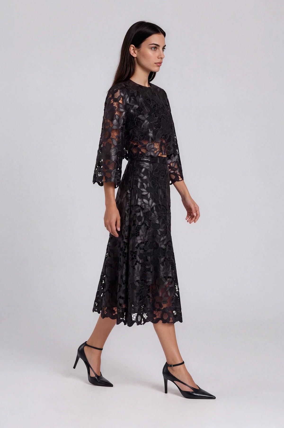 Model wearing black lace bell sleeve top with matching lace midi skirt, side view