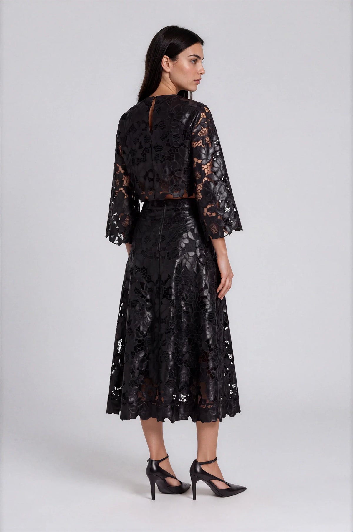 Back view of model wearing black lace bell sleeve top with matching midi skirt and heels.