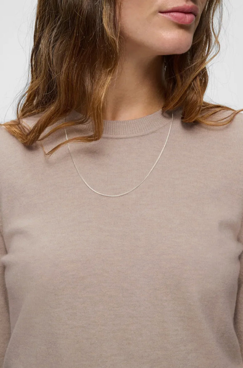 Woman wearing a light taupe crew neck knit pullover with a delicate chain necklace.