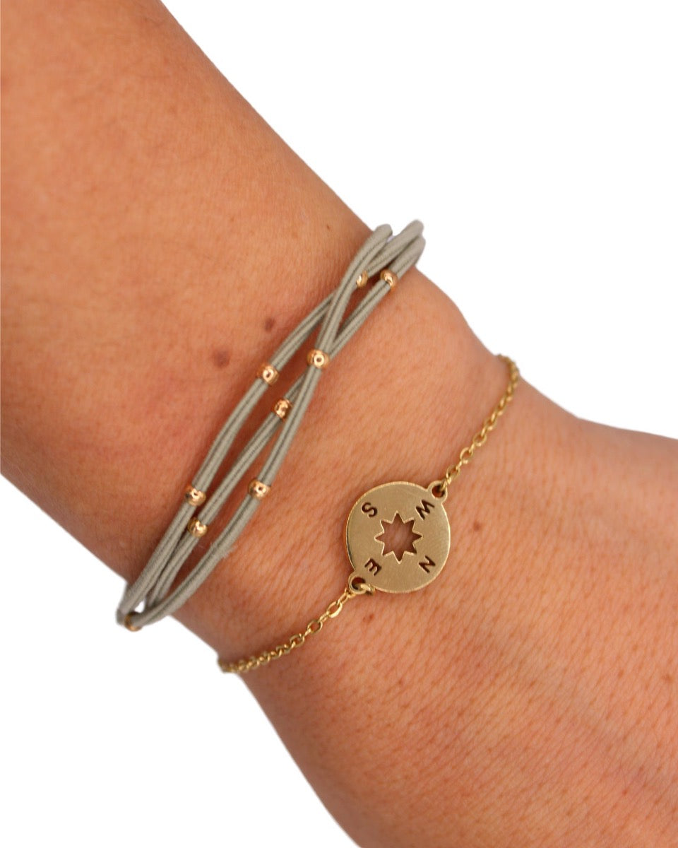 Gray multi-strand hair tie bracelet set with gold compass charm on wrist