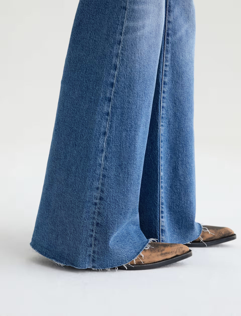 Wide-leg blue denim jeans with raw hem, worn with brown cowboy boots