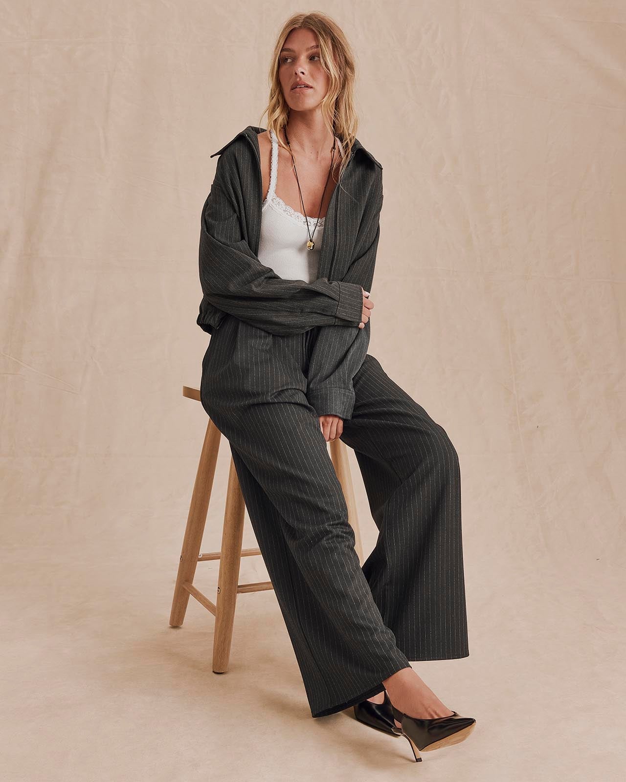 Model seated on stool wearing charcoal pinstripe oversized blazer jacket with wide-leg trousers