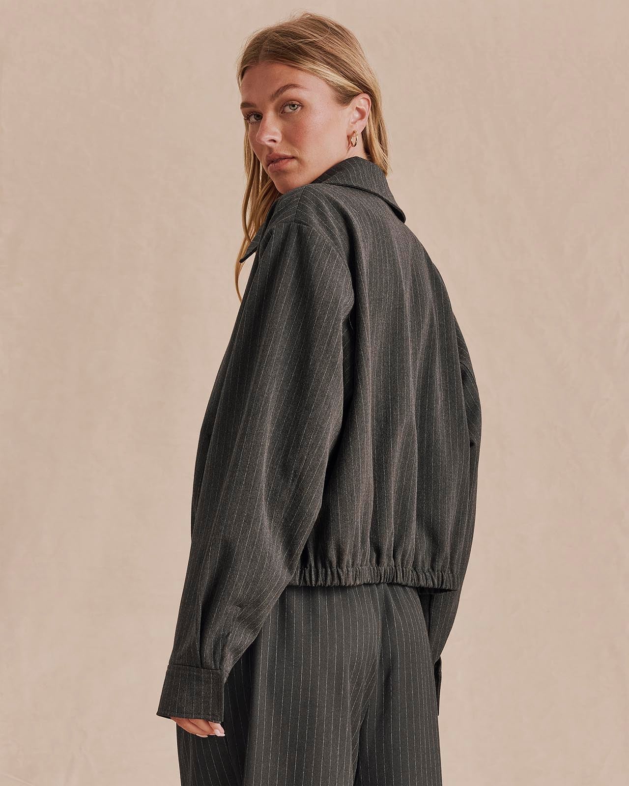 Back view of model wearing charcoal pinstripe cropped bomber jacket with elasticated hem