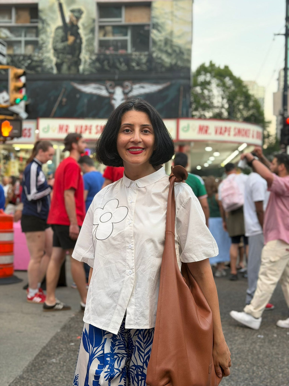 Woman wearing tan leather knot tote bag on busy urban street in summer
