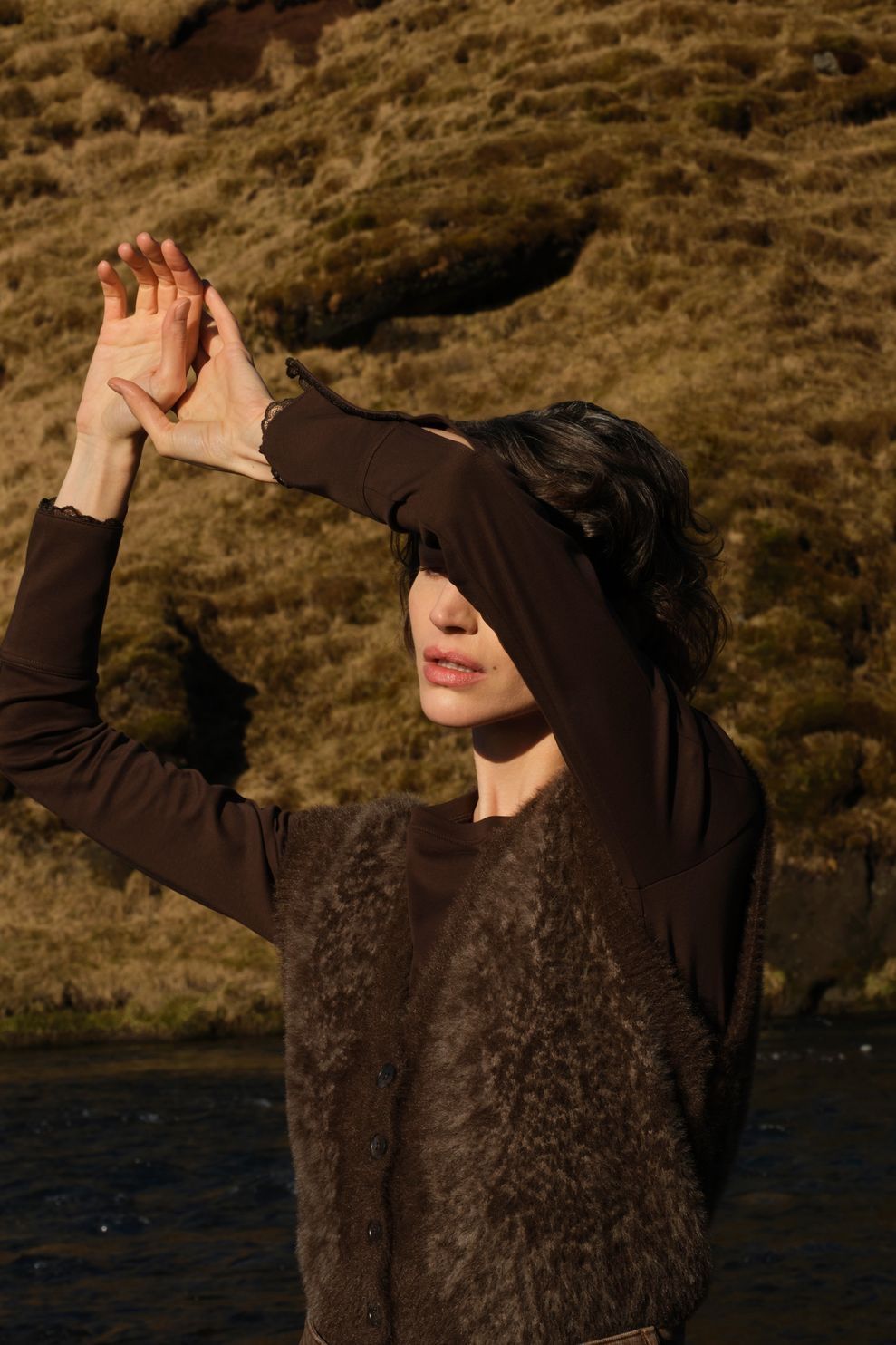 Dark brown sleeveless animal fur cardigan with button front, worn over long-sleeve top