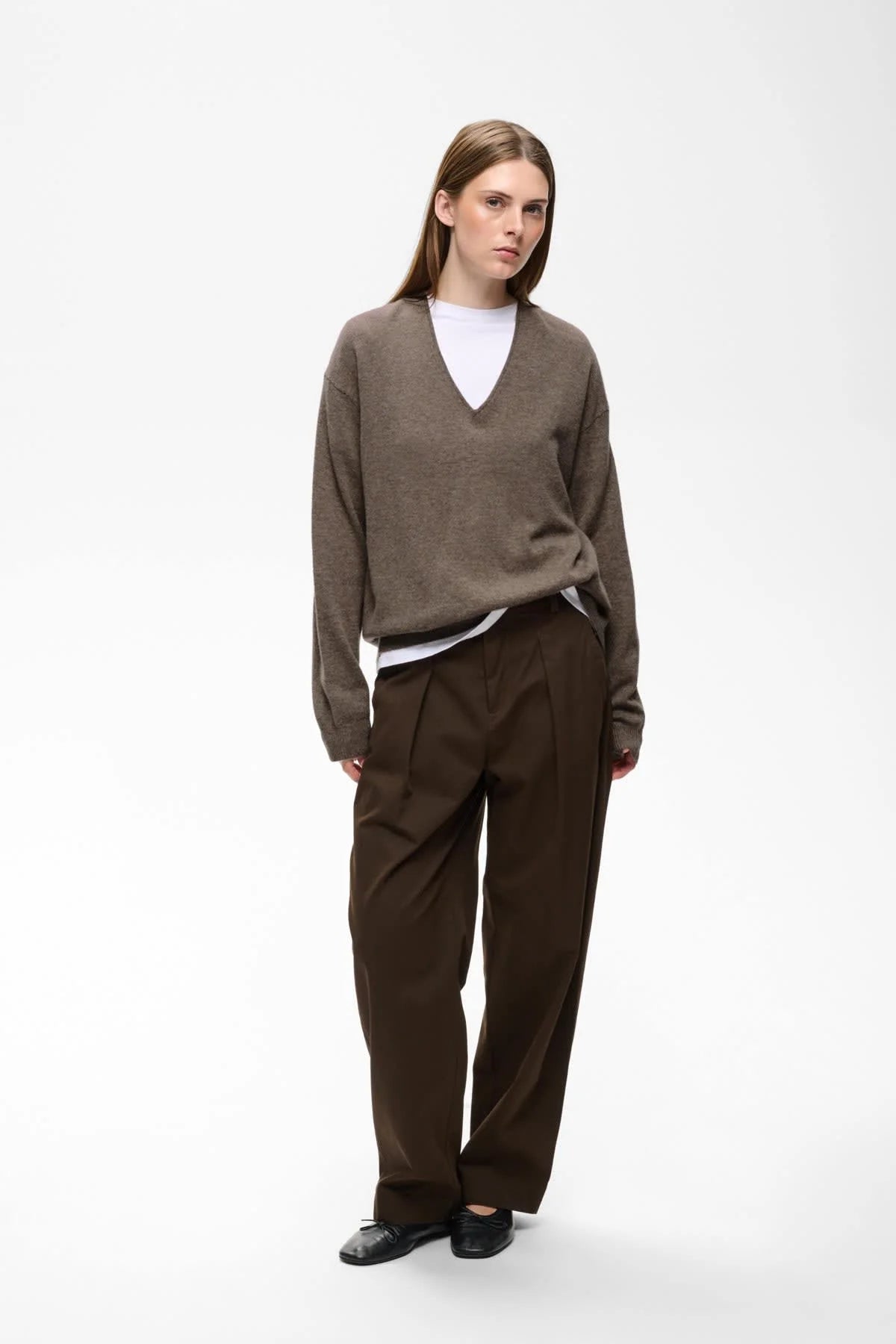 Taupe V-neck knit sweater worn over white tee with dark brown trousers