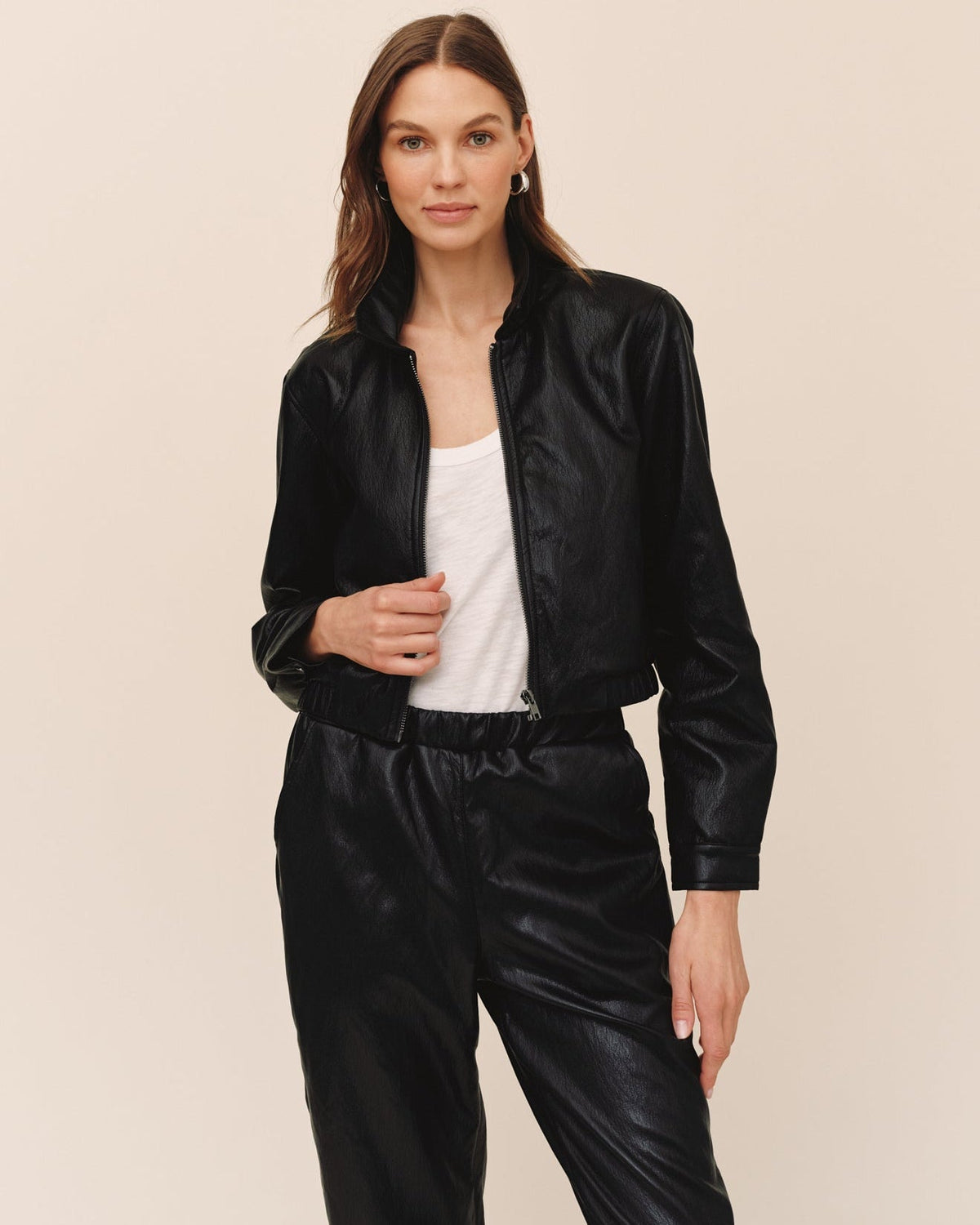 Woman wearing a black faux leather crop bomber jacket with zip closure, styled with matching black pants.