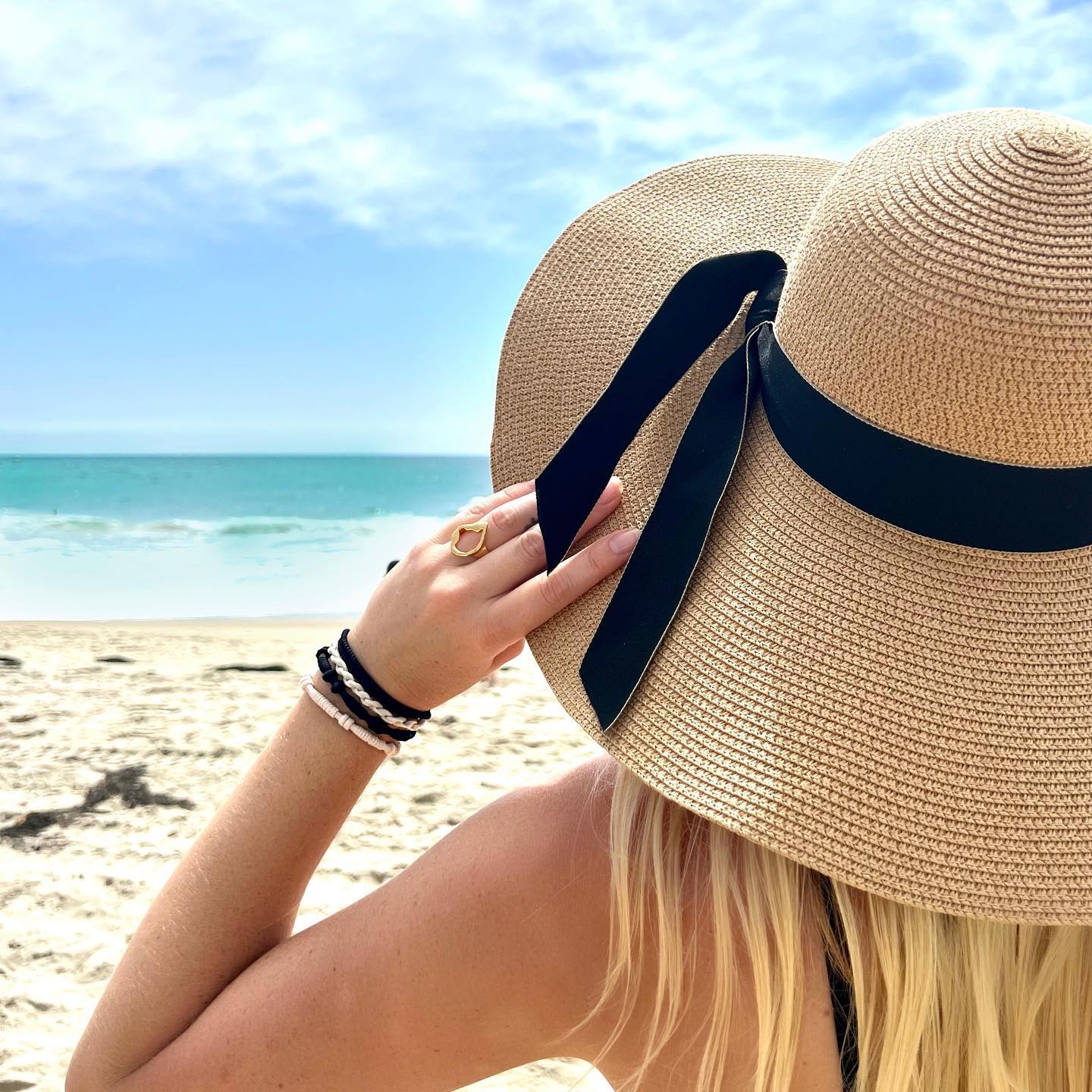 Model wearing Gypsea Bands Hairtie Tulum as bracelet stack at beach with straw hat