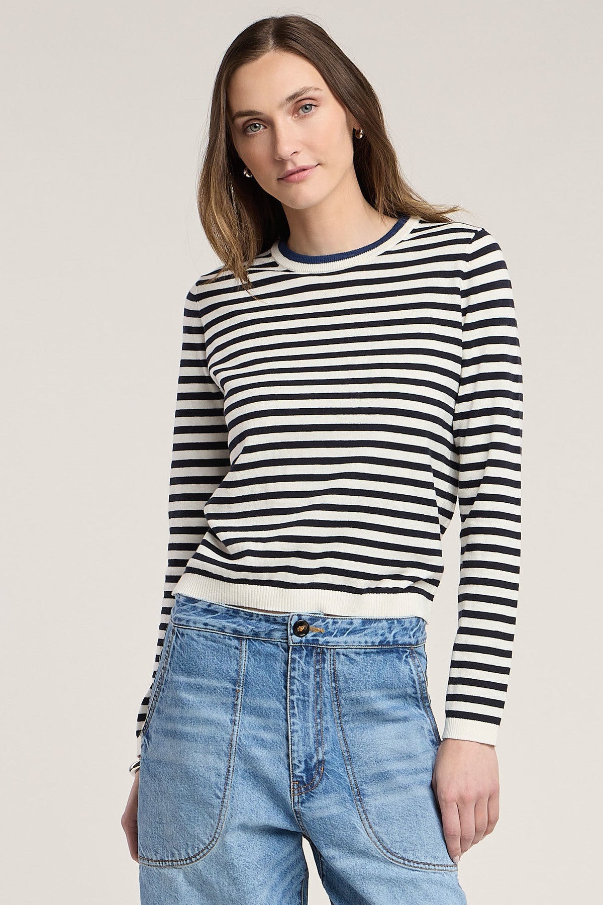 Woman wearing a navy and white striped long-sleeve crewneck sweater with light blue jeans