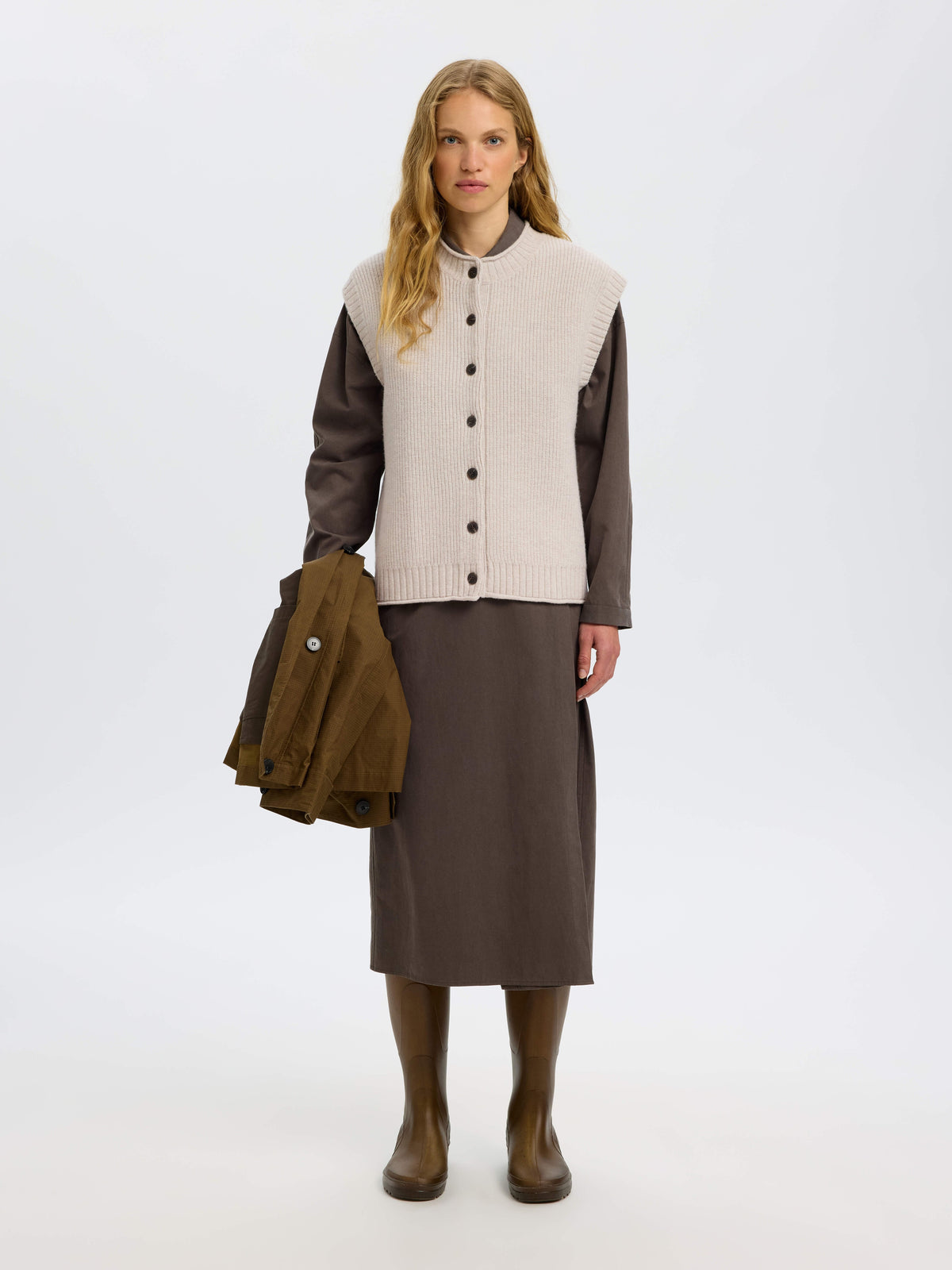Model wearing a light beige ribbed knit vest over a dark brown long-sleeve shirt and midi skirt