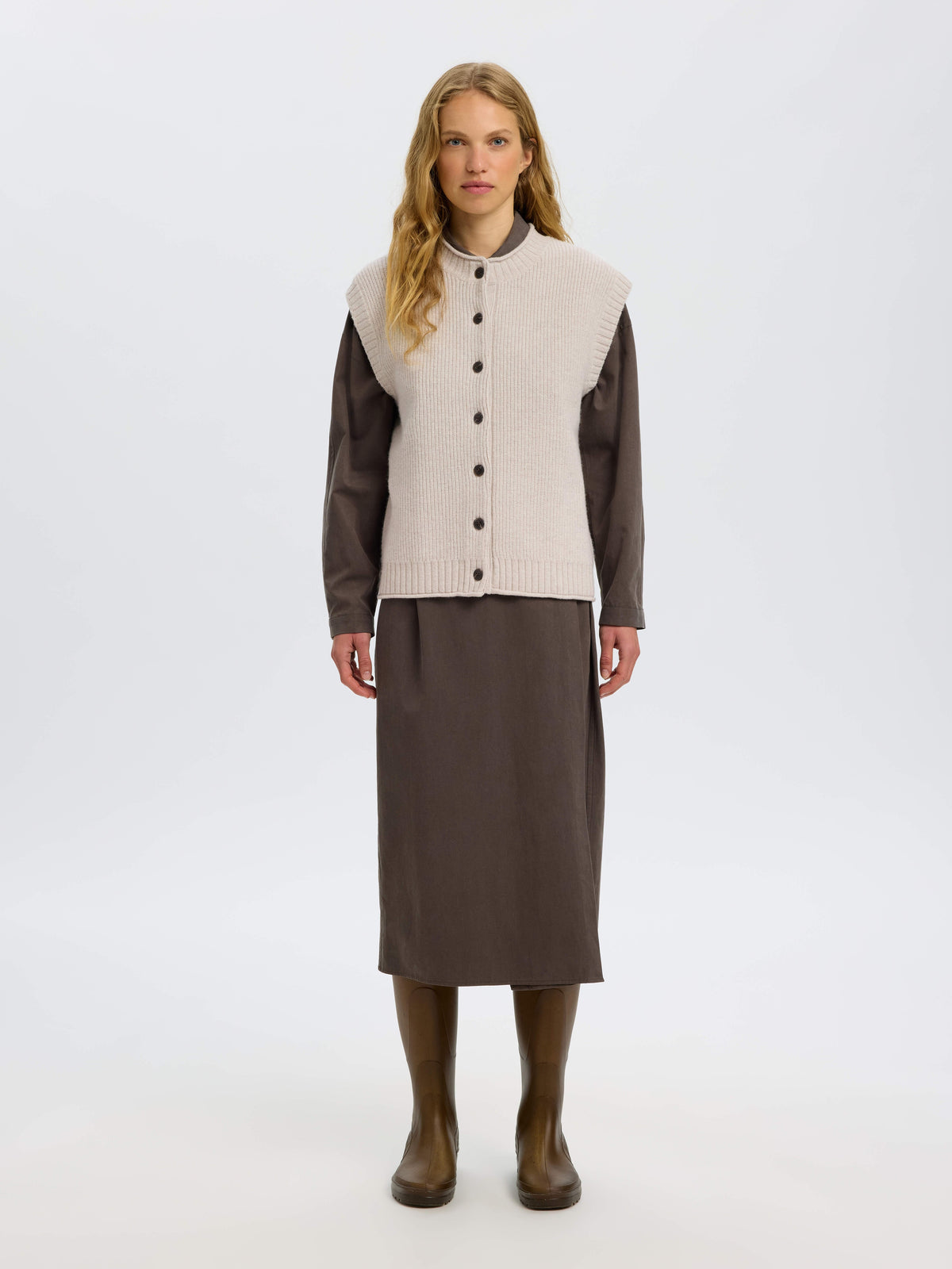 Model wearing Selected SLWNATHIA wool knit vest in Silver Birch over dark brown shirt and midi skirt