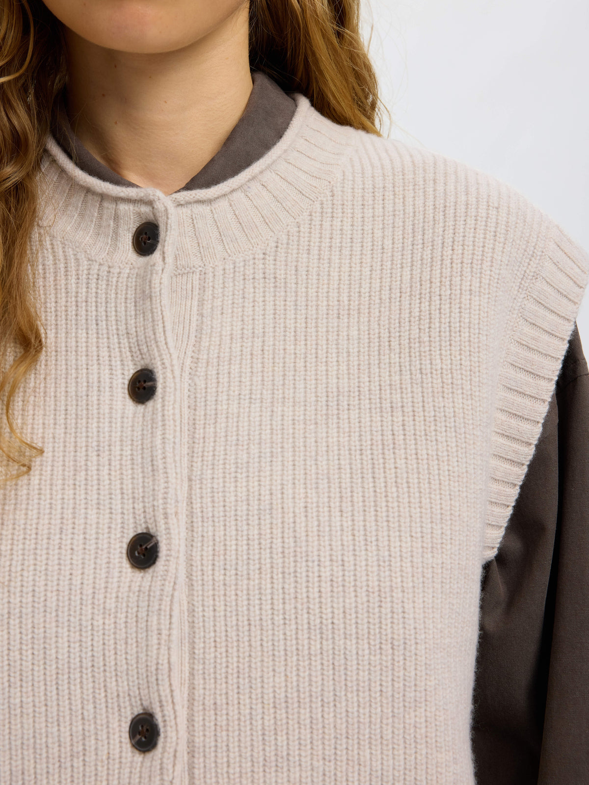 Close-up detail of cream ribbed knit vest with dark brown buttons and grey sleeves