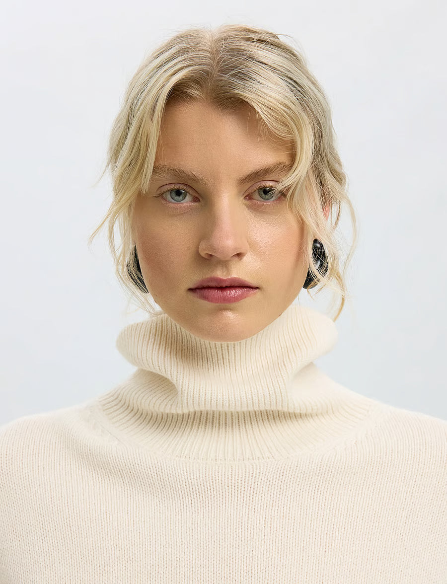 Cream ribbed knit turtleneck sweater with soft rolled collar, worn by blonde model