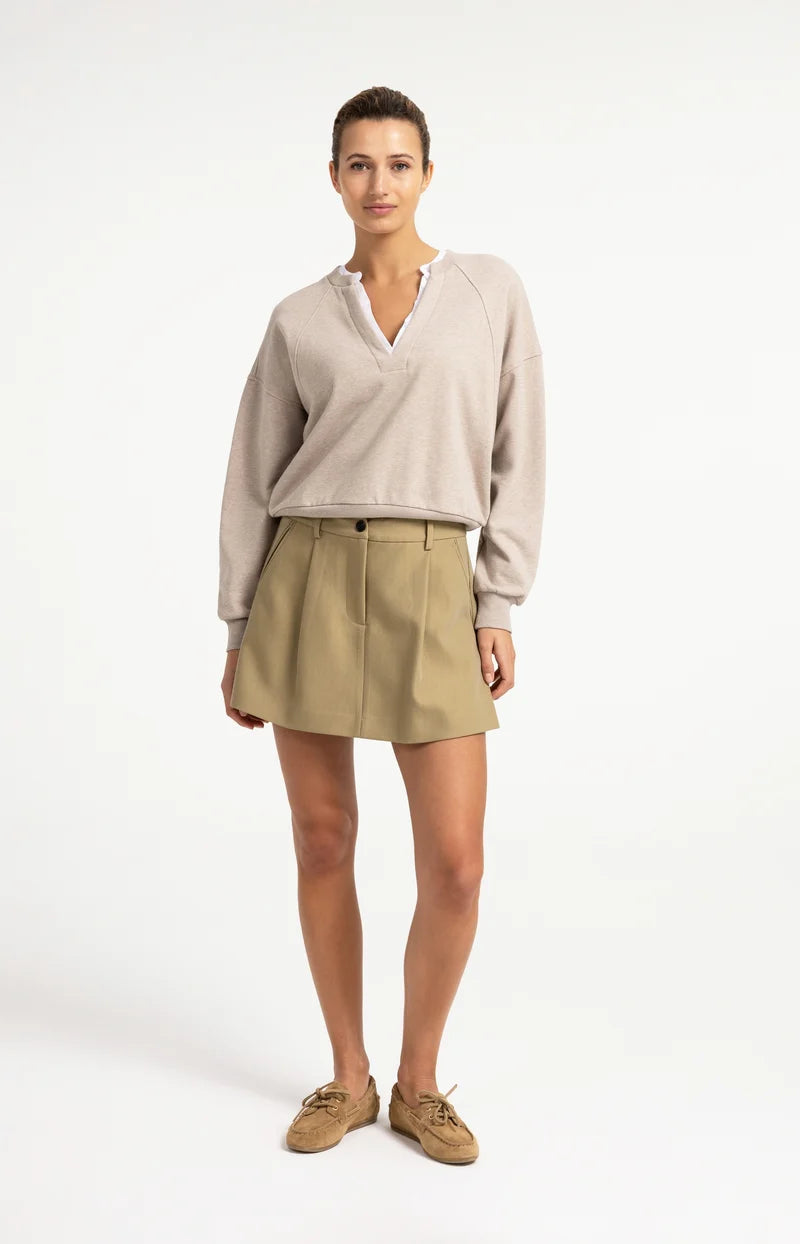 Beige oversized V-neck sweatshirt with white woven collar detail, worn with khaki mini skirt